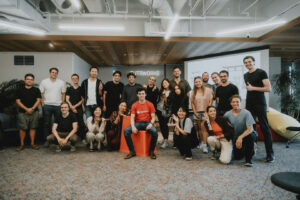 A large group of international FUTRFEST participants posing together under the FUTRWORKS neon sign in Umeda, Osaka