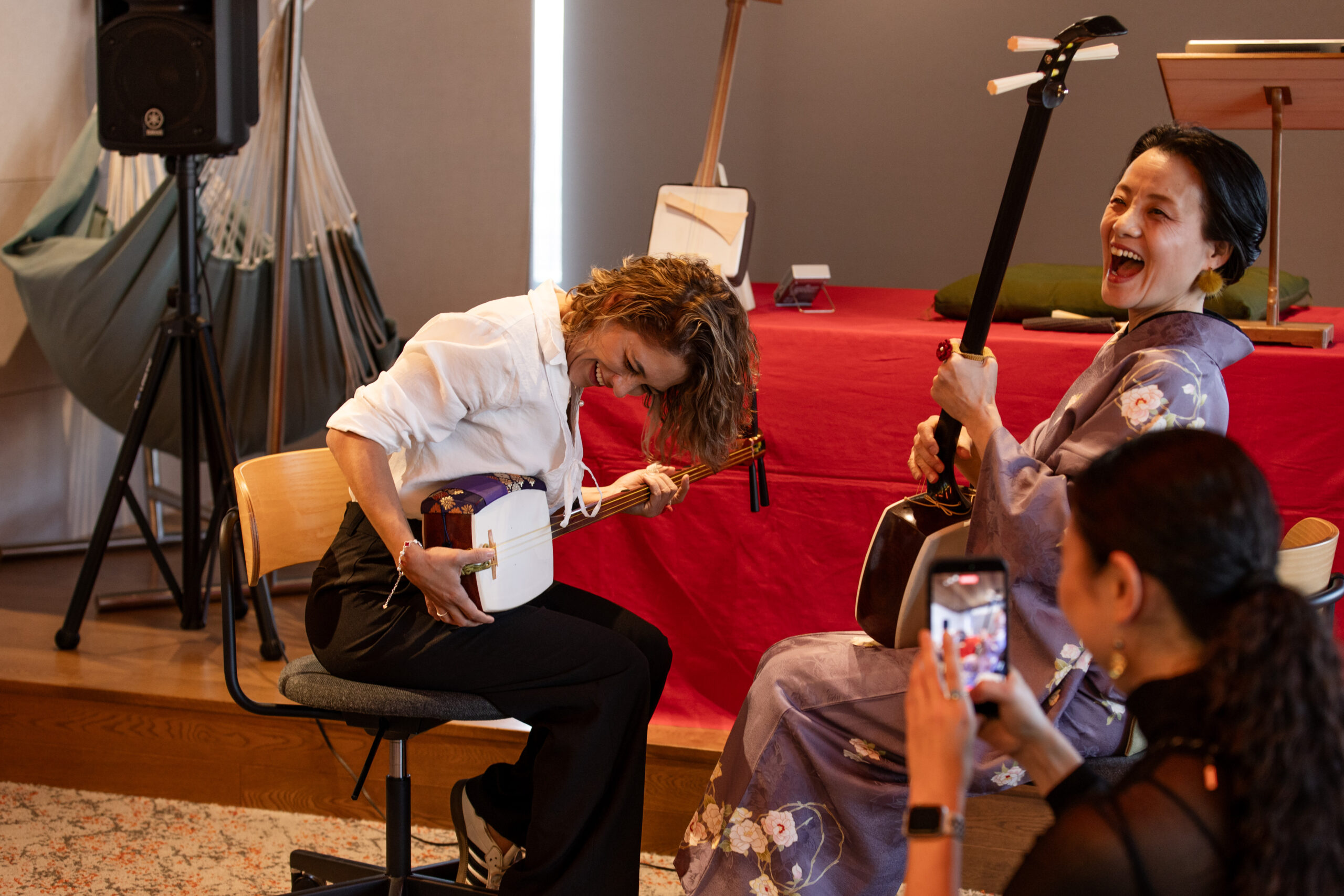 A participant tries the shamisen while a smiling instructor in a kimono teaches her